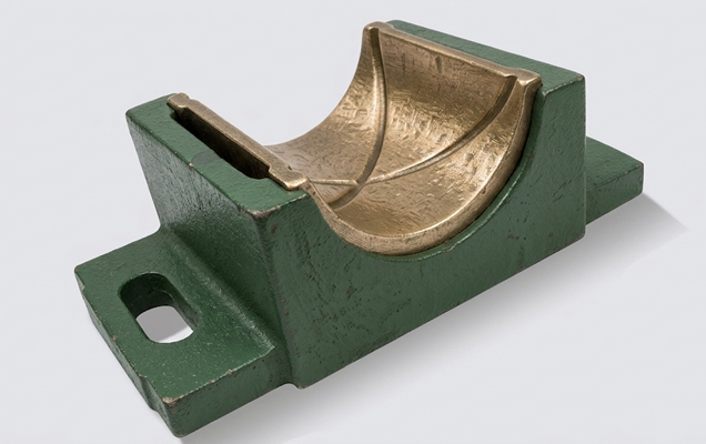 Conjunto de soporte industrial formado por una base de chumacera de hierro fundido pintada de verde y un inserto semicircular de bronce fundido con acabado texturizado. Vista superior isométrica sobre fondo gris.