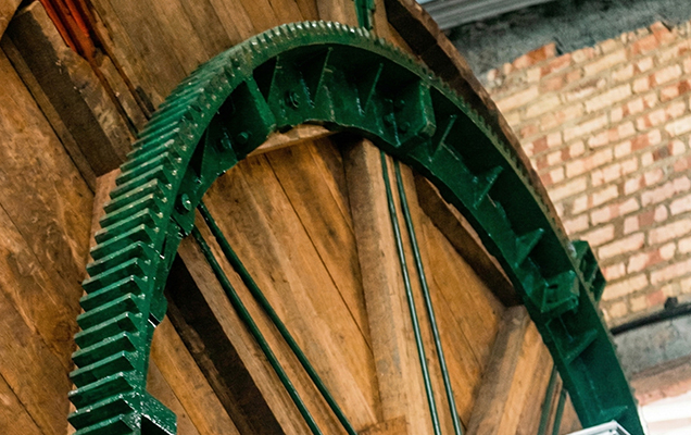 Detalle en primer plano de una gran cremallera de engranaje de metal montada en el exterior de un bombo de curtido de madera. La cremallera es parte del sistema de transmisión para el movimiento de rotación en el proceso de curtir pieles en una curtiembre